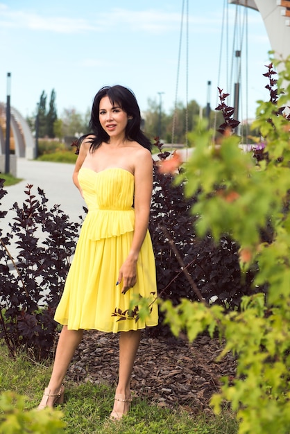 都市公園でポーズをとって黄色のドレスを着て官能的な女性ブルネット