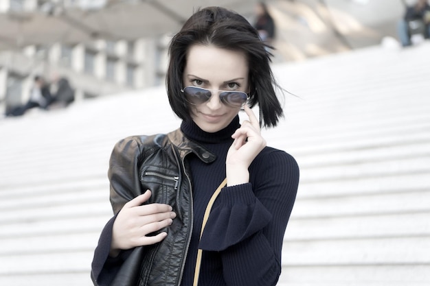 Sensual woman in sunglasses on stairs in paris, france, beauty. Woman with brunette hair in black clothes, fashion. Ambition, challenge, success. Fashion, accessory, style. Beauty, look, hairstyle.