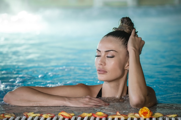 Sensual woman touching wet hair in pool