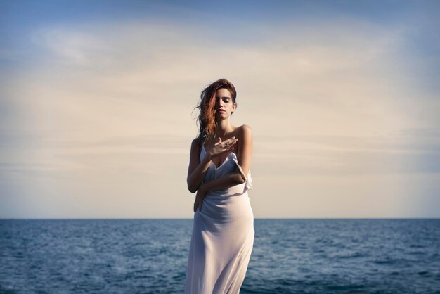 Sensual young female standing on seashore with closed eyes