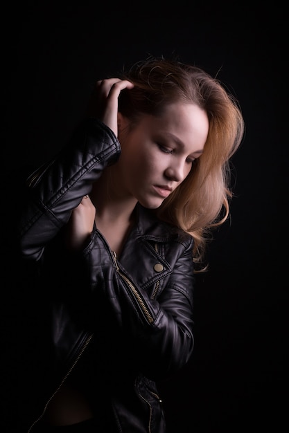 Sensual young model with lush wavy hair, wears leather jacket, posing with shadow on her face