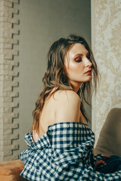 Sensual young woman with a naked back in a plaid shirt looks over her shoulder