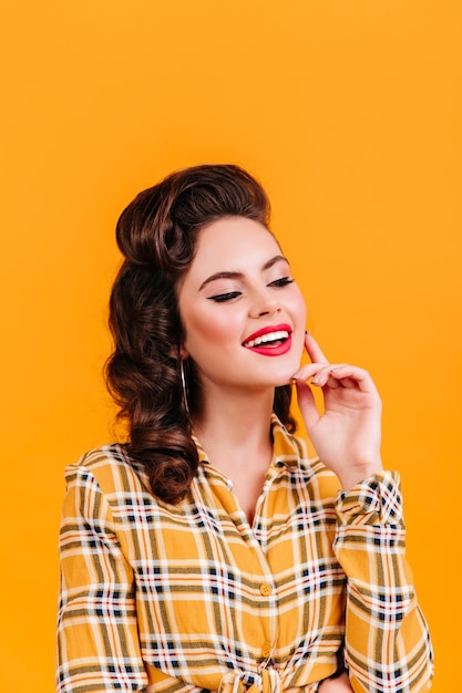 Sensual young woman with wavy hairstyle posing on yellow background Studio shot of playful pinup girl in vintage checkered shirt