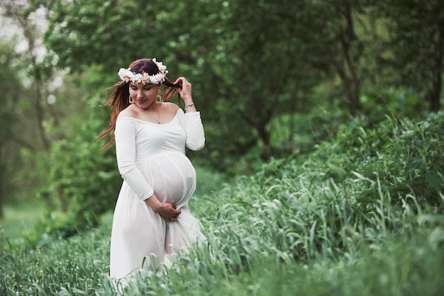 Sensuality and care. Beautiful pregnant woman in dress have a walk outdoors. Positive brunette