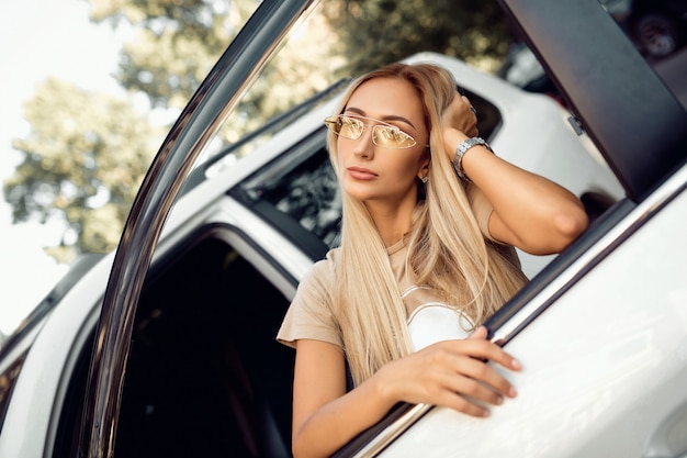 Sensuele blonde in stijlvolle kleding poseren in een mooie auto. Auto's en meisjes