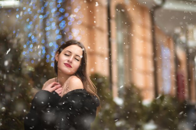 sensuele brunette vrouw met blote schouders poseren in de buurt van de kerst showcase decoratie met slingers. Ruimte voor tekst