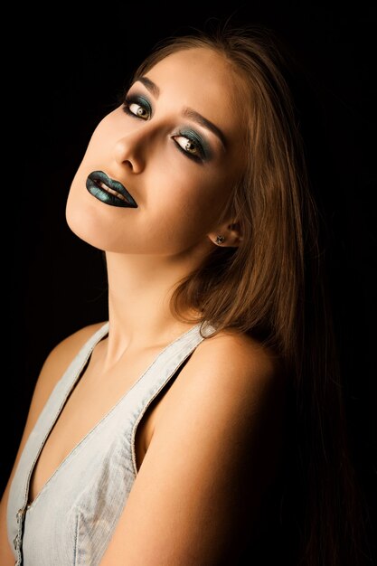 Sensuele brunette vrouw met perfecte huid en creatieve metallic groene make-up. Close-upportret in studio op een donkere achtergrond