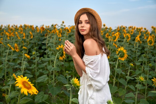 Sensuele vrouw in strohoed en witte jurk die zich voordeed op het veld