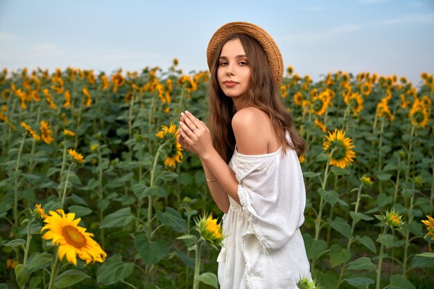 Sensuele vrouw in strohoed en witte jurk die zich voordeed op het veld