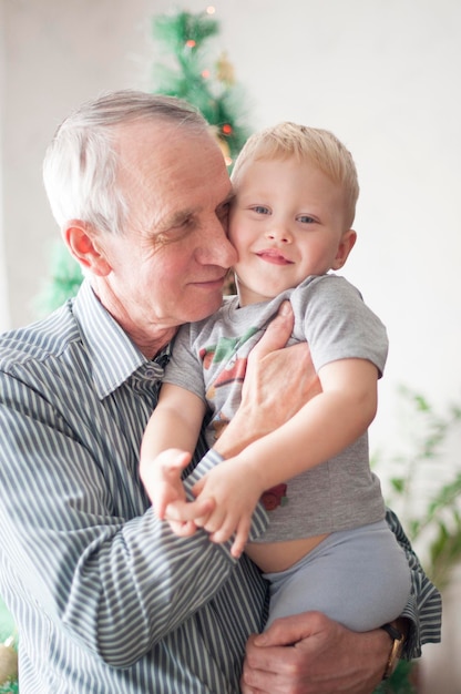 Foto vecchio sentimentale che tiene un bambino nelle braccia davanti all'albero di natale decorato