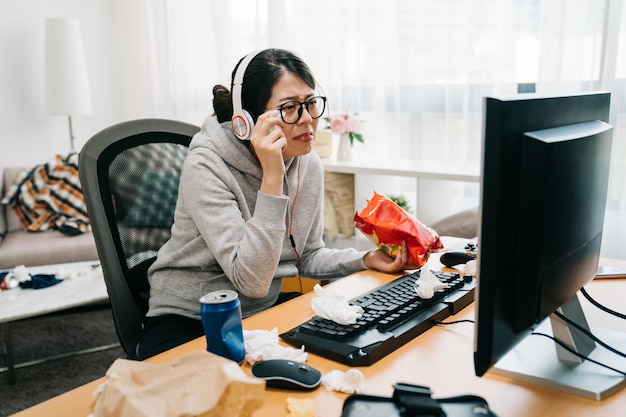 Sentimental woman crying and wiping tears with napkin while watching dramatic film movie. lazy female homebody at home binge watch series on computer in messy room eating unhealthy junk food chips