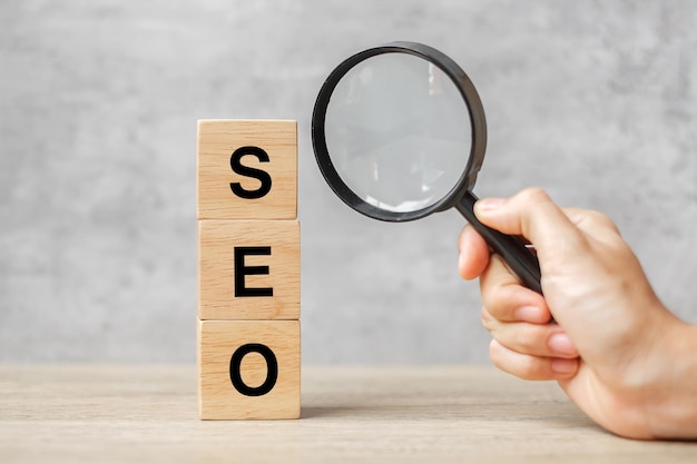 Seo (search engine optimization) testo blocchi di legno cubo e mano che tiene la lente d'ingrandimento sul tavolo. idea, strategia, pubblicità, marketing, parola chiave e concetto di contenuto