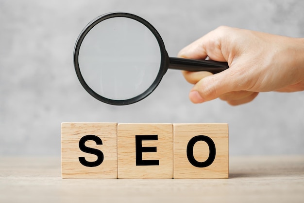 Seo (search engine optimization) testo blocchi di legno cubo e mano che tiene la lente d'ingrandimento sul tavolo. idea, strategia, pubblicità, marketing, parola chiave e concetto di contenuto