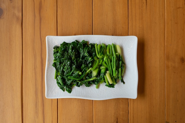 Seperate slided and boiled Chinese (Thai) KALE vegetable lay on the white rectangle on the wood table.