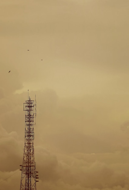 Sepia image of telecommunication tower against cloudy sky