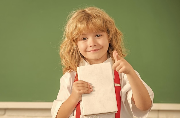 9月1日学校に戻って本のポイントの指の幸せな十代の少年を持つ子供時代の発達の子供教育の知識の日の概念黒板で長い髪のオタクの子供