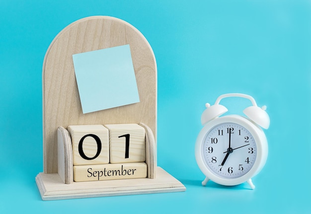 September 1 on a wooden cubic calendar next to an alarm clock
on a blue background the first day of the autumn month