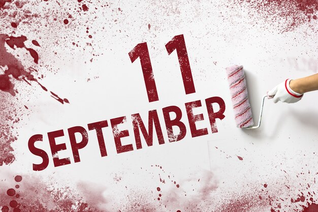 9月11日。月の11日目、カレンダーの日付。手は赤いペンキでローラーを保持し、白い背景にカレンダーの日付を書き込みます。秋の月、年の日の概念。