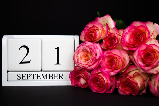 Photo september 21 wooden calendar white on a black background pink roses lie nearby copy space holiday