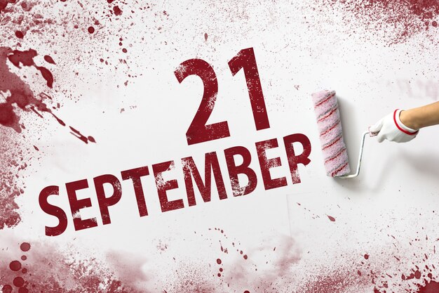 September 21st . day 21 of month, calendar date. the hand holds\
a roller with red paint and writes a calendar date on a white\
background. autumn month, day of the year concept.