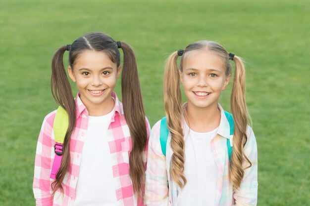 September. Vacation is over. Back to school. Cute schoolgirls with long ponytails. Ending of school year. Cheerful smart schoolgirls. Happy schoolgirls outdoors. Small schoolgirls with backpacks.