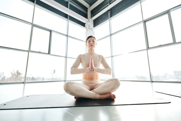 Sereen meisje in activewear zittend in pose van lotus op mat tijdens ontspanningsoefening