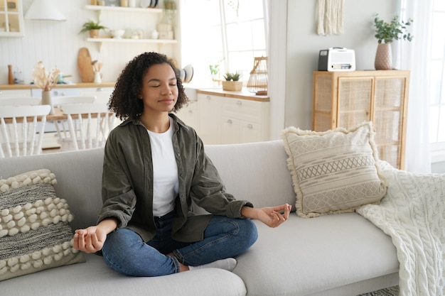 Photo a serene black woman meditates on a couch eyes closed in a sunlit stylish living room