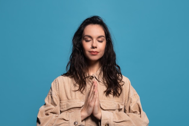 Serene calm young european brunette woman in casual with closed eyes praying or meditating