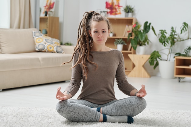 Serena ragazza in activewear attraversando le gambe mentre è seduto sul pavimento e pratica rilassante esercizio di yoga