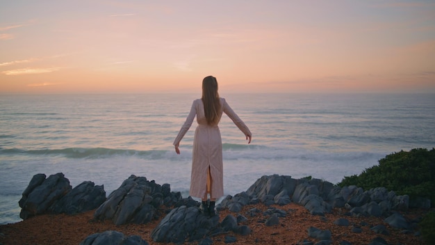 Serene girl enjoying sunset nature raising hands back view woman looking marine