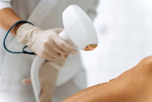 Serene lady getting depilation of legs in cosmetology center. Assistant holding special gadget in arms. Stock photo