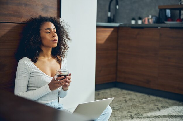 写真 お茶を飲みながら家具にもたれかかる穏やかな女性