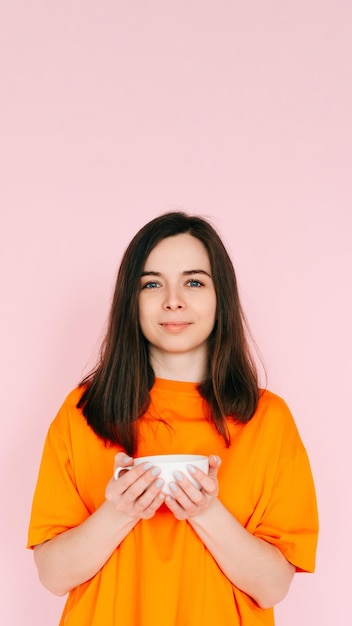 Serene Leisure Charming Woman in Orange Attire Savoring a Delightful Drink in a Mug Relishing Fr