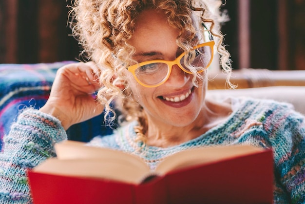 Foto persone serene che si rilassano e svolgono attività ricreative in casa leggendo un libro con copertina rossa education concept lifestyle una donna felice che legge un romanzo seduta a casa una signora sorridente che si diverte