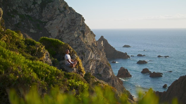 Serene persoon die mediteert met uitzicht op de oceaan Rustige man die yoga beoefent op een klif