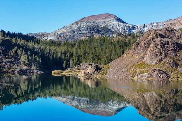 Serene scene by the mountain lake with reflection of the rocks in the calm water.