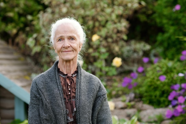 Serene senior woman with white hair standing in front of camera in the garden