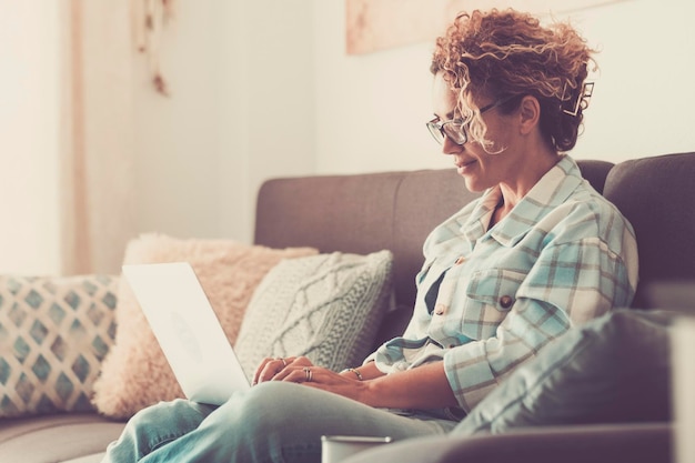 Serene volwassen vrouw met behulp van laptop glimlachend op de bank in ontspanning en comfort indoor home vrijetijdsbesteding Gelukkige vrouwelijke mensen surfen op het web op de computer met verbinding Modern huis levensstijl