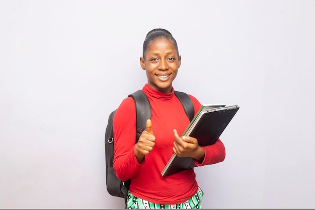 ノートパソコンと本を手に横に立っている穏やかな若い10代の女子学生