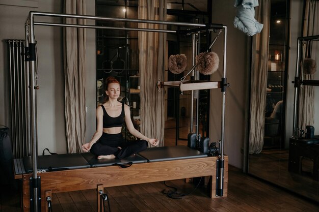 Premium Photo  Serenity in motion a redhead woman in a black outfit  meditates on a pilates reformer in a tranquil studio setting