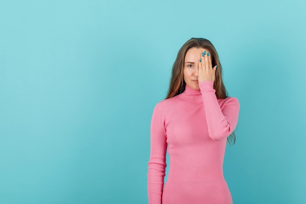 Serieus blond meisje bedekt rechteroog met hand op blauwe achtergrond