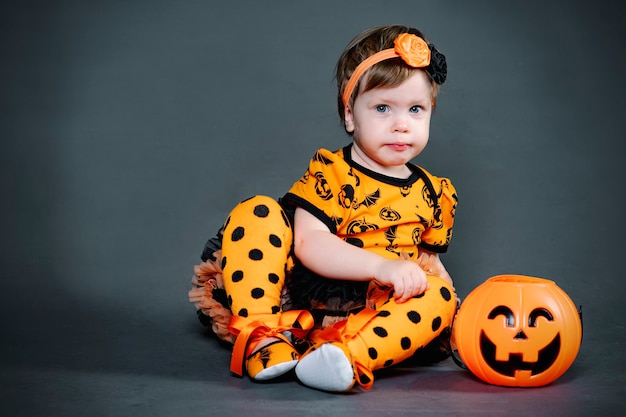 Serieus, klein meisje in Halloween-kostuum met pompoensnoepkom. Grappig kind in de studio, grimas en horror tijdens de vakantie.