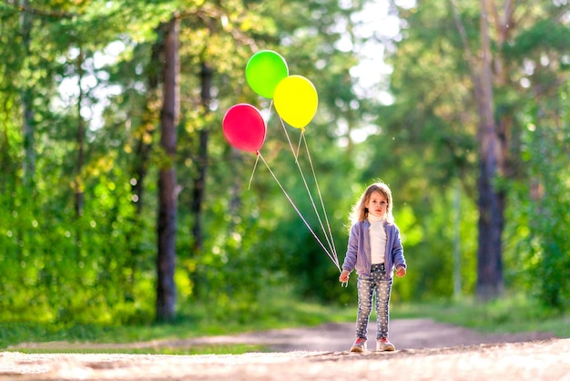 Serieus meisje met heldere ballonnen in het zomerbos