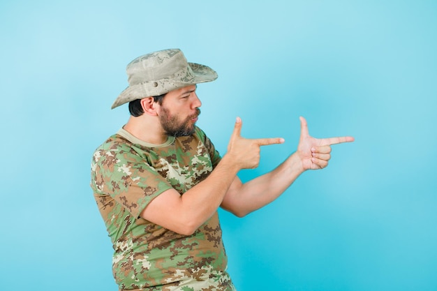 Foto serieus, officier toont een pistoolgebaar door recht op een blauwe achtergrond te kijken