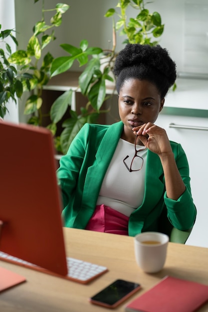 Serieuze Afro-Amerikaanse vrouw marketeer zit aan tafel met computer en kopje koffie in thuiskantoor