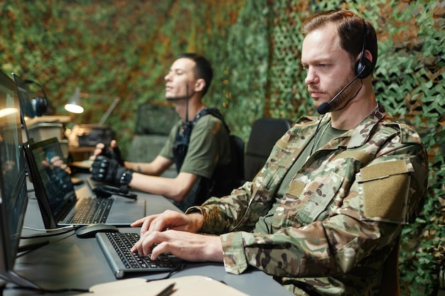 Serieuze jonge mannelijke operator in camouflage uniform die op het toetsenbord tikt