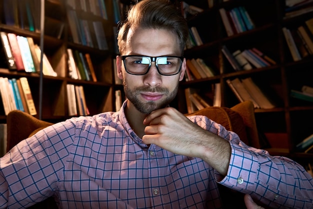 Foto serieuze jonge zakenman die naar een camera of computer webcam kijkt, laat werkt, online videoconferentie leert, belt of webinar kijkt op het kantoor thuis bij nachtlamplicht, webcam view, headshot