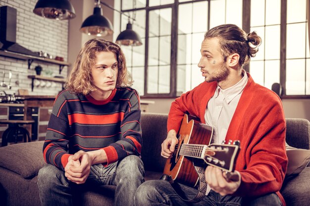 Foto serieuze man. ernstige blonde man luistert naar zijn muziekleraar die gitaar bij hem speelt