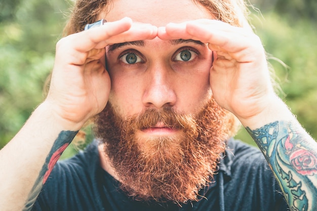 serieuze man met baard kijkt door zijn handen zeer geconcentreerd