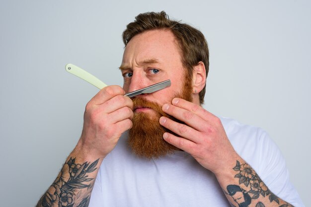 Serieuze man met mes is gefocust op het knippen van zijn baard